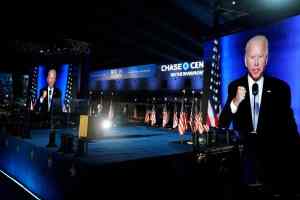 unidec stage for the Biden Harris event. Biden is on stage and projected onto large video walls on either side of the stage. Lots of american flags line behind Biden. The stage is covered in a blue rug and had a blue with white stars fascia on the front. televised event.