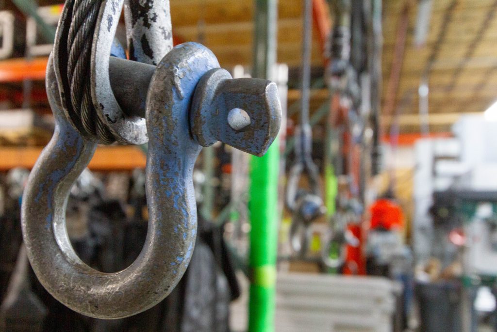 a shackle hangs in the foreground with blurred out rigging accessories in the background