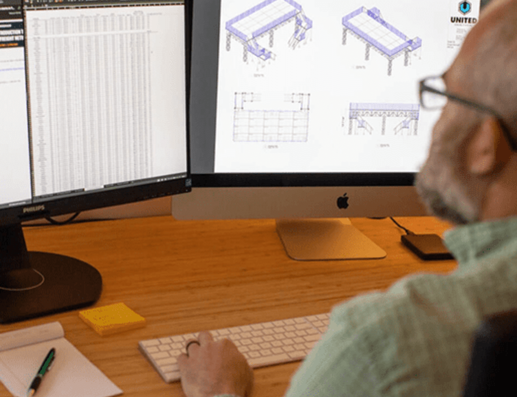 eric frishman sitting at a computer working on vectorworks designs while doing project management for an event structure