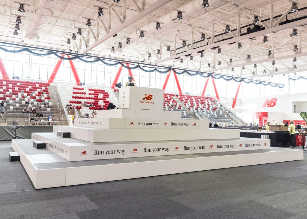 Custom riser pyramid with while fascia and New Balance logos around it, inside the center of The Track at New Balance in Boston, MA
