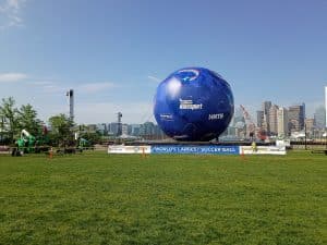 Guiness Worold Record holding largest soccer ball outside on a green field. Soccer ball is blue with white letters of sponsors, most predominantly Masport who sponsored this sturcture. The ball sits on a platform in the middle of the field.