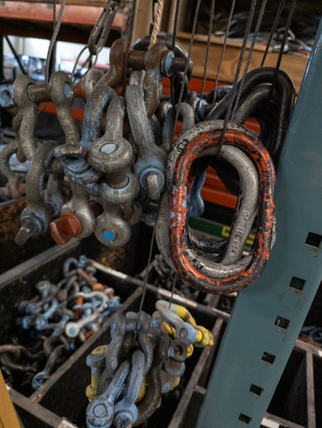 shackles and masterlinks hanging in a warehouse in front of bins of other rigging accessories