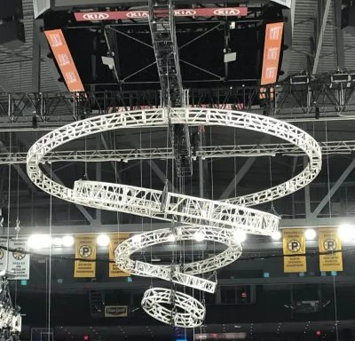 Multiple circular trusses hanging at various angles, with the diameter of each truss shrinking as the hang lower, creating a vortex or tornado shape. Circle trusses are hooked to automation motors in a mother truss "X" above it.