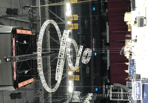 Multiple circular trusses hanging at various angles, with the diameter of each truss shrinking as the hang lower, creating a vortex or tornado shape. Circle trusses are hooked to automation motors in a mother truss "X" above it.