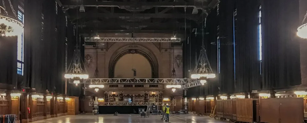 Black drape, which is attached to truss that lines the perimeter of teh cieling, hang down covering up the hall windows, blacking out the hall from natural light.