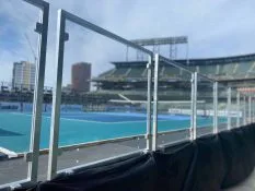 Close up of plexiglass safety rails on a stage with black skirting hanging down. It is outdoors at a stadium. The stage is a blue colored court.