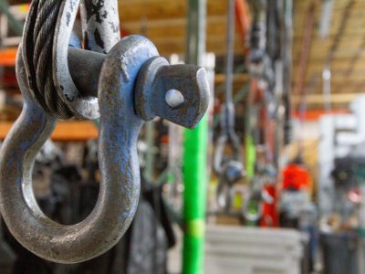 a shackle hangs in the foreground with blurred out rigging accessories in the background