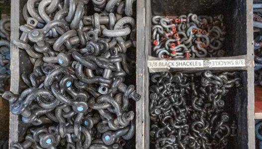 Looking down into a wooden box with a long rectagular partition on the left and two smaller square partitions on the right. Inside each partition section are a different size of shackle, put into "knuckles" (groups of 5).
